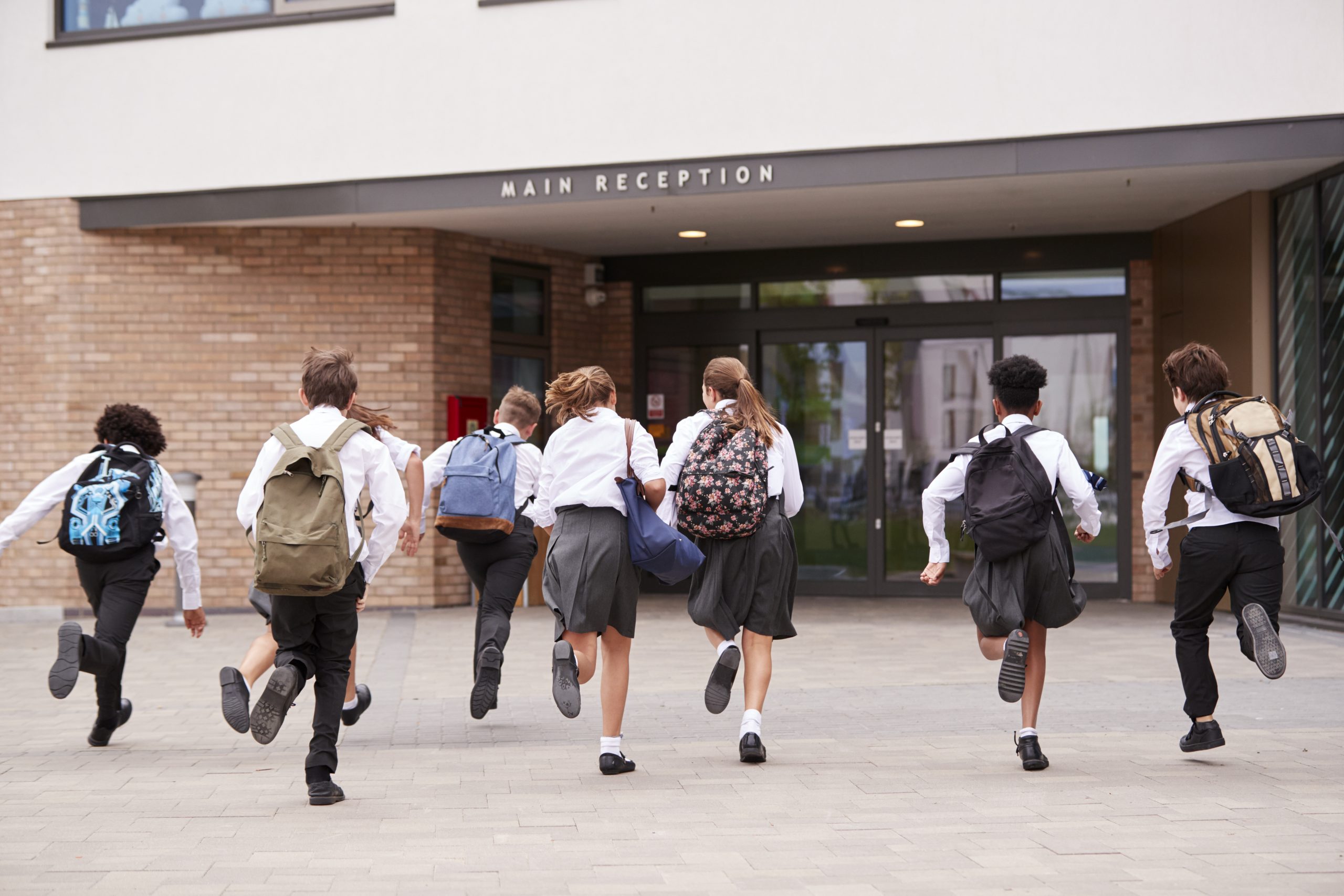 group of high school students wearing uniform running into school building at beginning of class